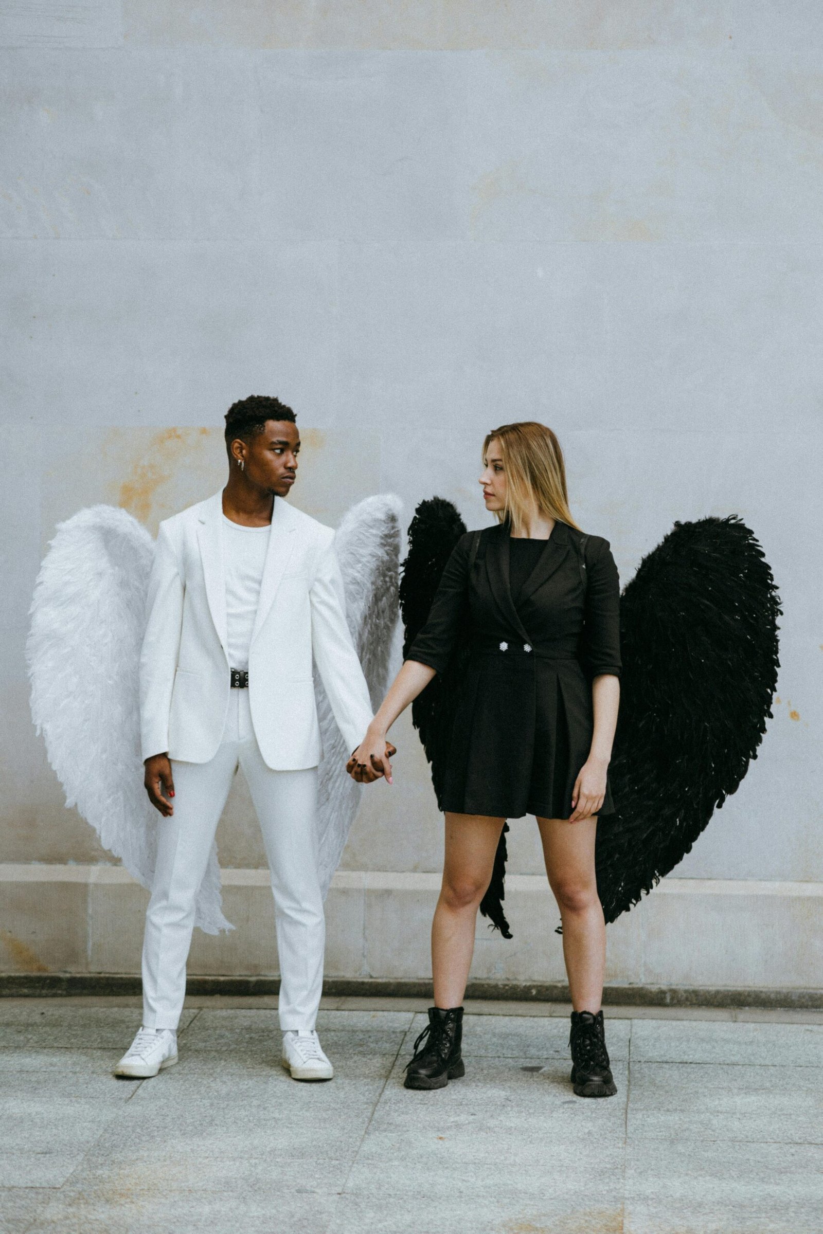 A couple in contrasting angel and devil outfits symbolizing unity and duality.
